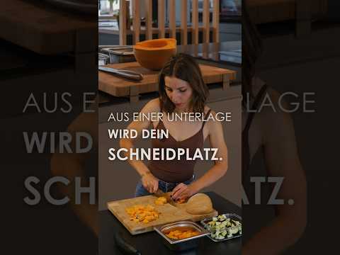 Anwendung der modularen SchnittKnecht® Schneidebrett-Unterlage: Edelstahlkomponenten auseinanderziehen, vorhandenes Schneidebrett auflegen und an den Anschlagleisten ausrichten. Rutschhemmende Silikonprofile stabilisieren die Auflage. Geschnittene Zutaten werden direkt in einen passenden Küchenbehälter geschoben.