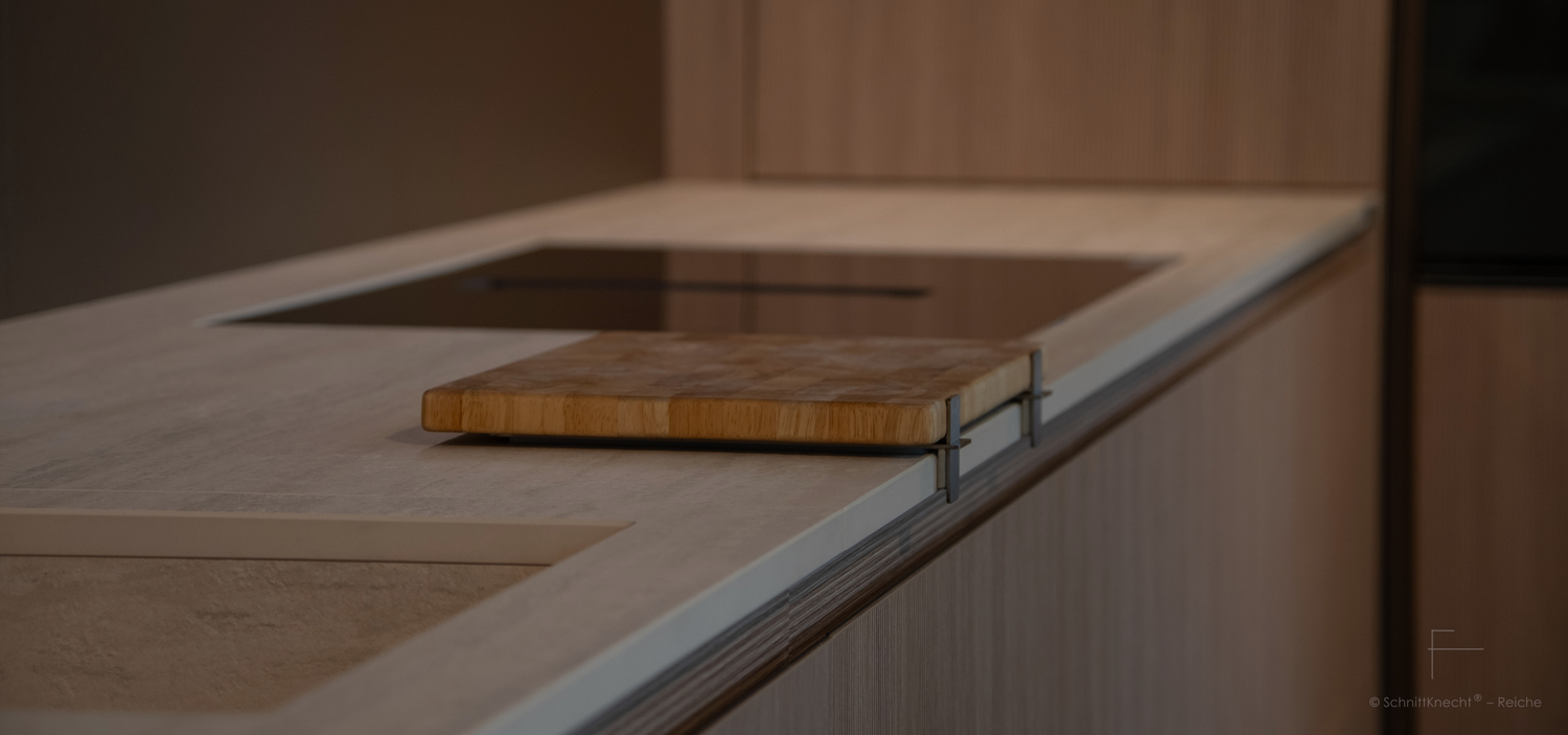 SchnittKnecht® Premium Schneidebrettunterlage aus Edelstahl und spülmaschinengeeignetem Silikon mit Schneidebrett in moderner heller Küche mit geriffelten Walnuss-Holzfronten und heller Steinplatte, elegant, natürlich und minimalistisch.