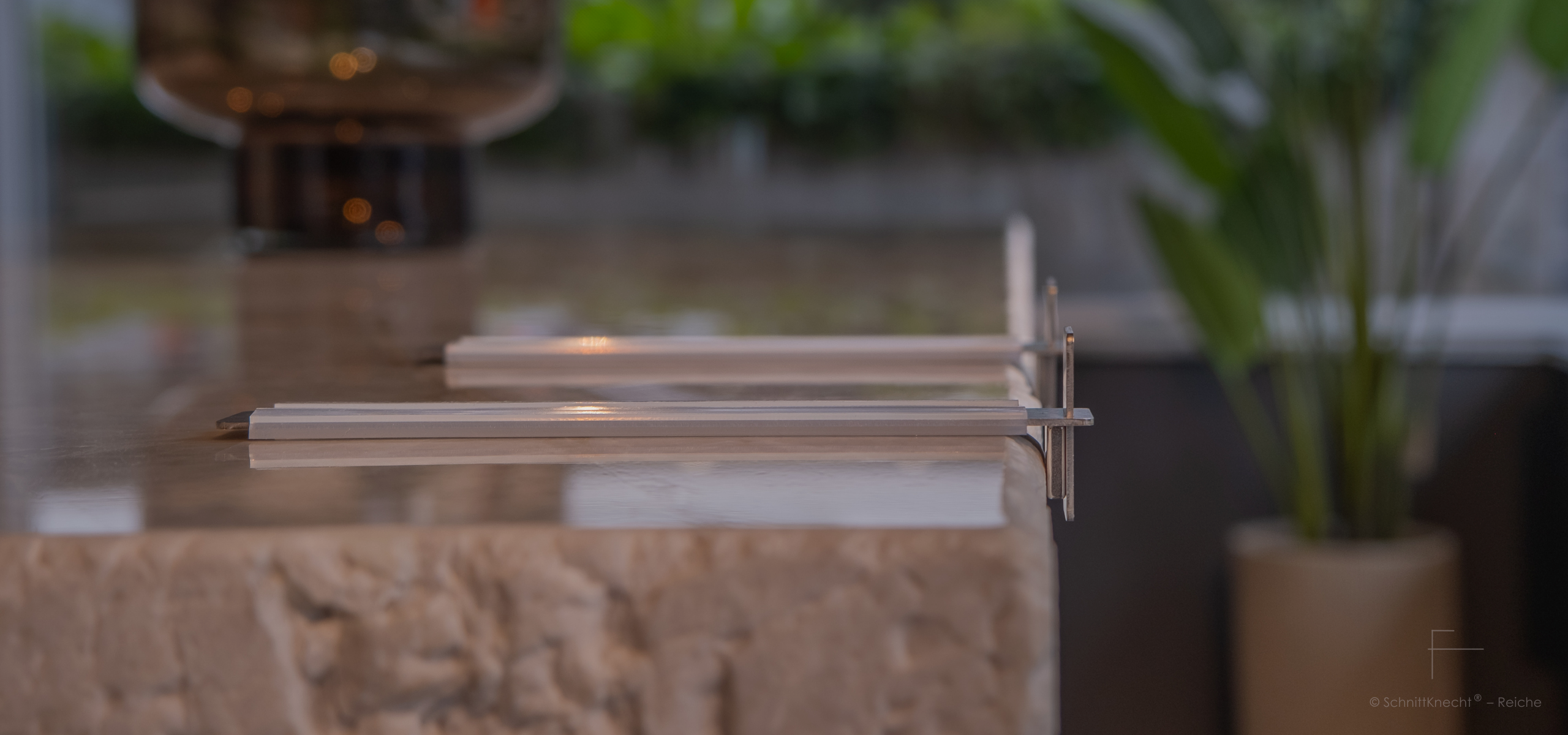 SchnittKnecht® Premium Schneidebrettunterlage aus Edelstahl und spülmaschinengeeignetem Silikon in moderner hochwertiger Küche auf massiver Arbeitsplatte aus hellem Stein mit gebrochener Steinkante.