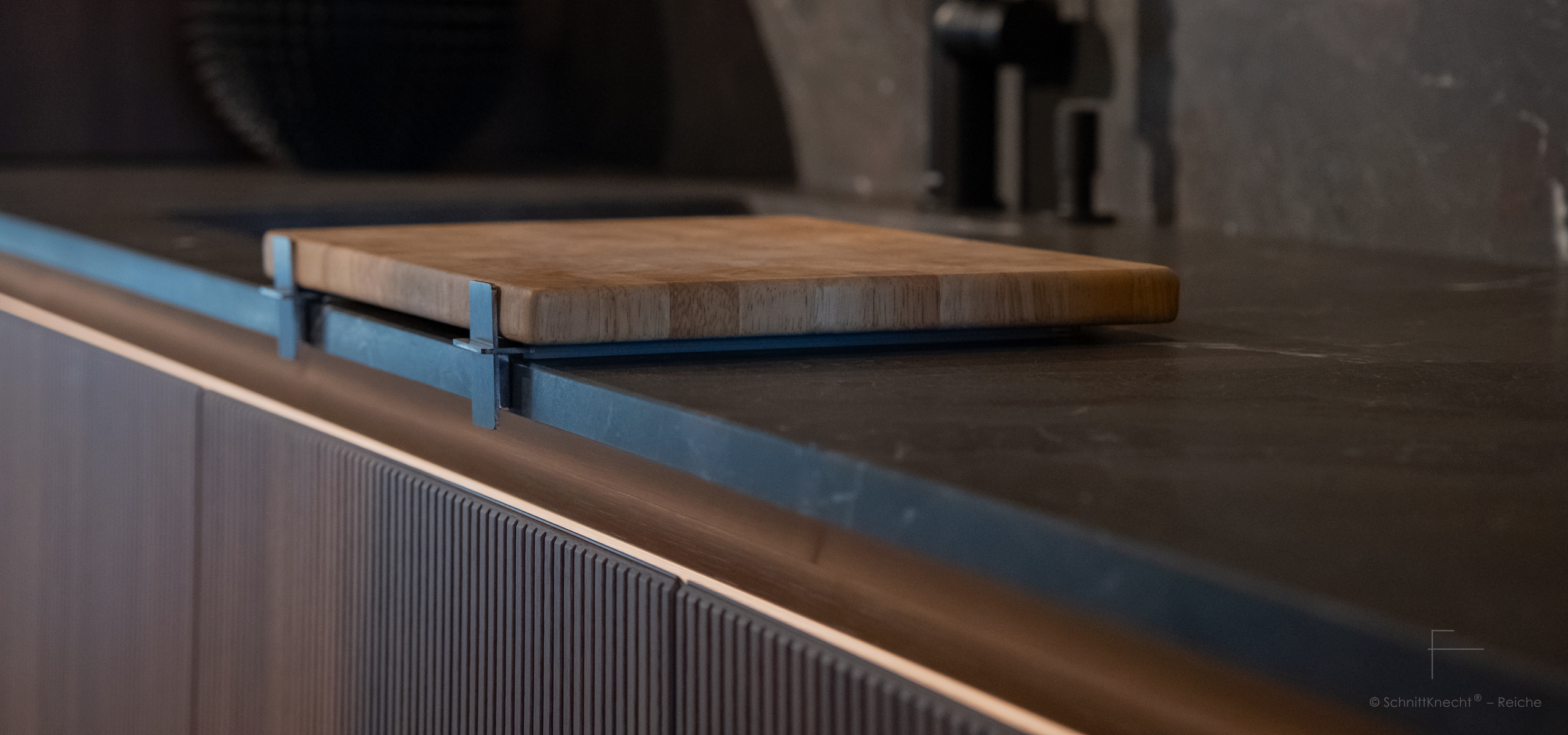 SchnittKnecht® Premium Schneidebrettunterlage aus Edelstahl und spülmaschinengeeignetem Silikon mit Schneidebrett in moderner dunkler Küche mit geriffelten Holzfronten und eleganter LED-Leiste.