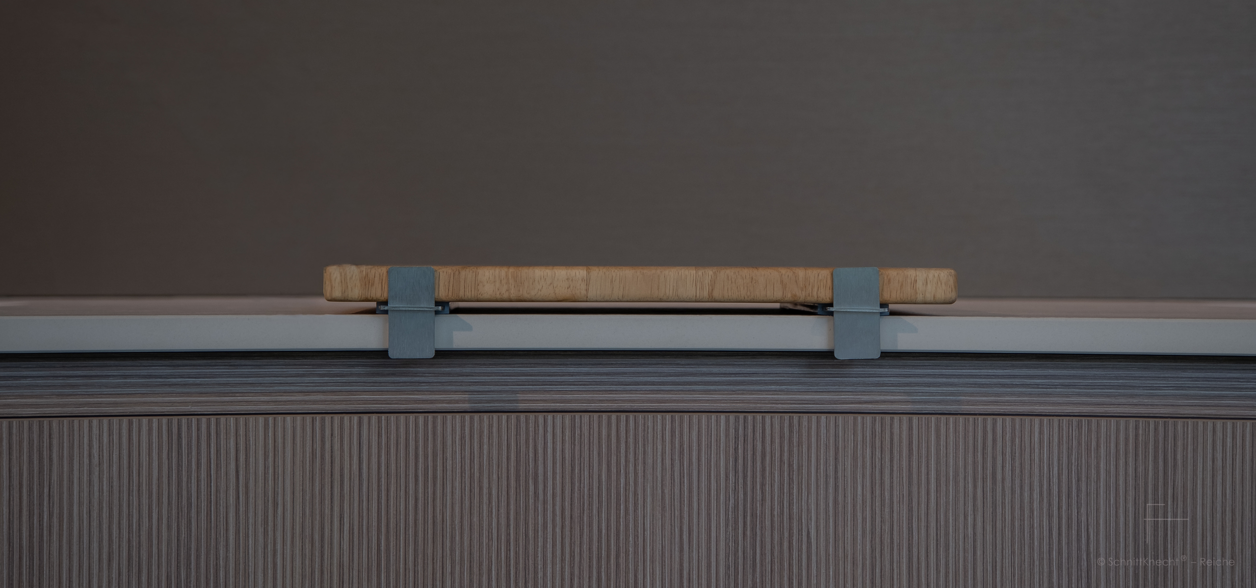 SchnittKnecht® Premium Schneidebrettunterlage aus Edelstahl und spülmaschinengeeignetem Silikon mit Schneidebrett in moderner heller Küche mit geriffelten Walnuss-Holzfronten und heller Steinplatte, Frontalansicht.