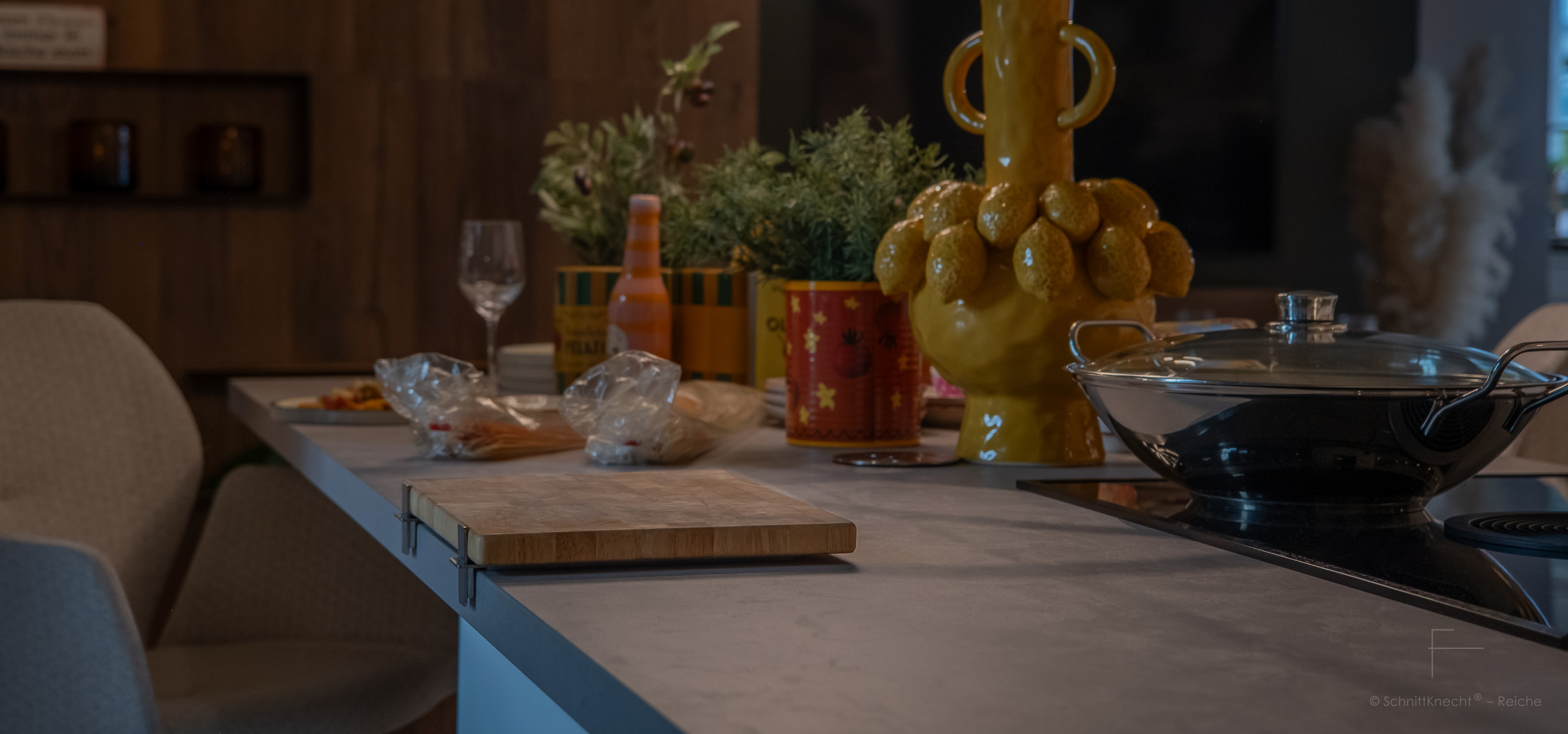 SchnittKnecht® Premium Schneidebrettunterlage aus Edelstahl und spülmaschinengeeignetem Silikon mit Schneidebrett in moderner Küche im toskanischen Stil, dekoriert mit Pasta, frischen Kräutern, Soßen, Weingläsern und Wok.