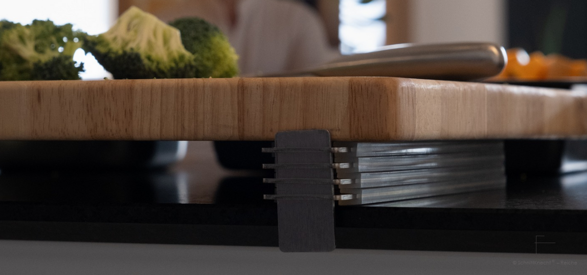 SchnittKnecht® Schneidebrett-Unterlage mit Ergonomie-Modulen und Holzschneidebrett auf dunkler Arbeitsplatte.