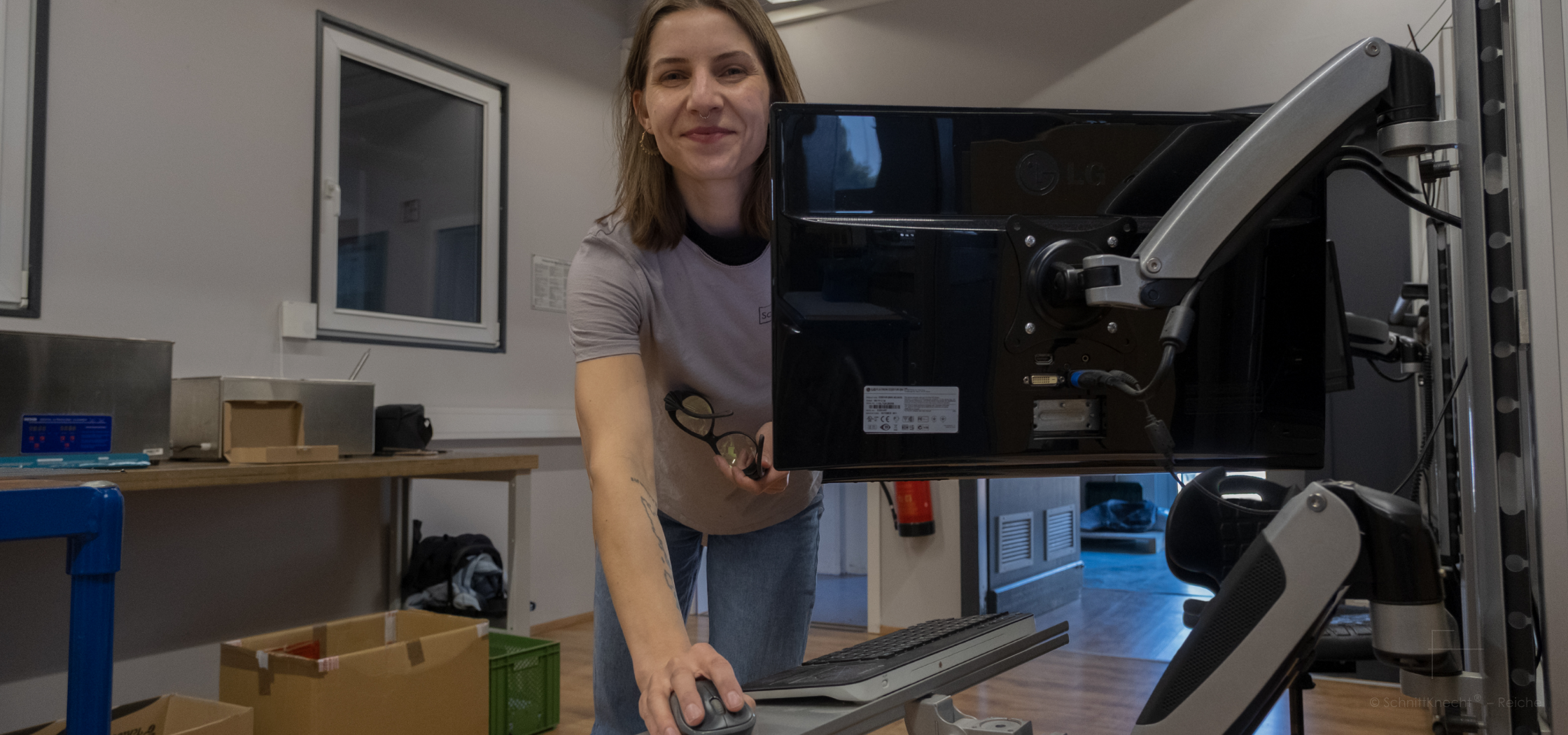 SchnittKnecht® Gründerin Caroline Reiche in der Fertigung am Arbeitsplatz. Sie arbeitet an einer Maschine und blickt in die Kamera – Einblick in die Entwicklung und Herstellung der Kücheninnovation aus Bayern.