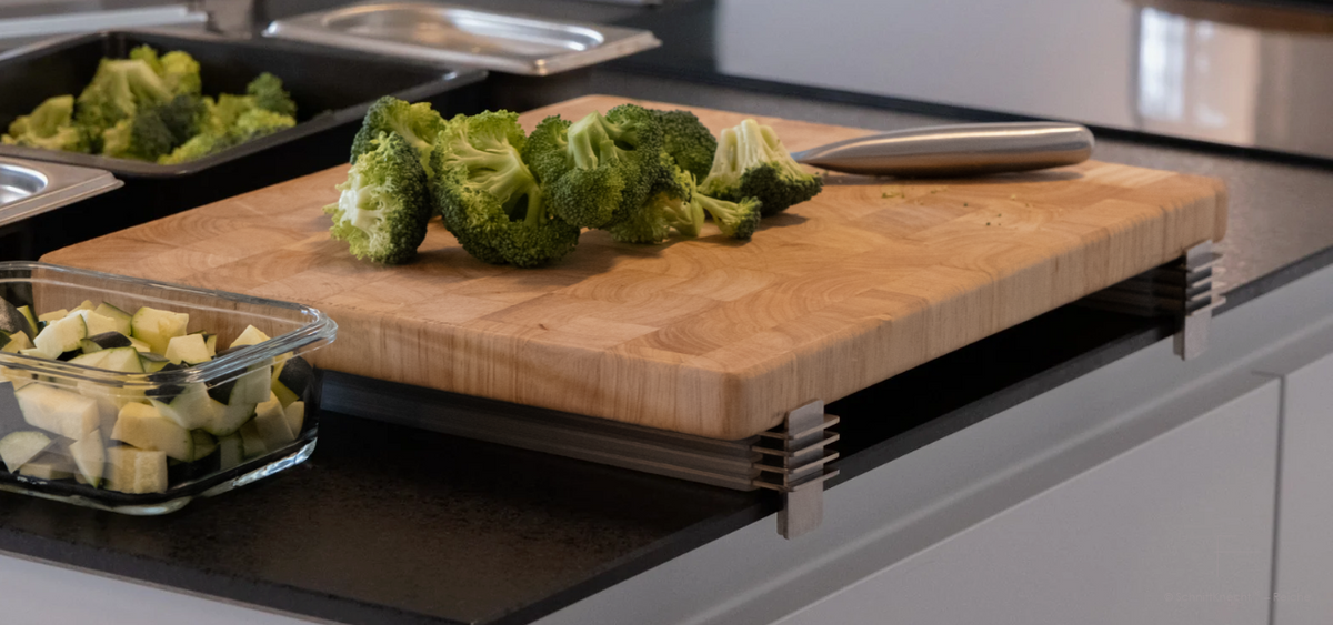 SchnittKnecht® Schneidebrett-Unterlage mit Ergonomie-Modulen und Holzschneidebrett auf dunkler Arbeitsplatte in moderner Designküche.