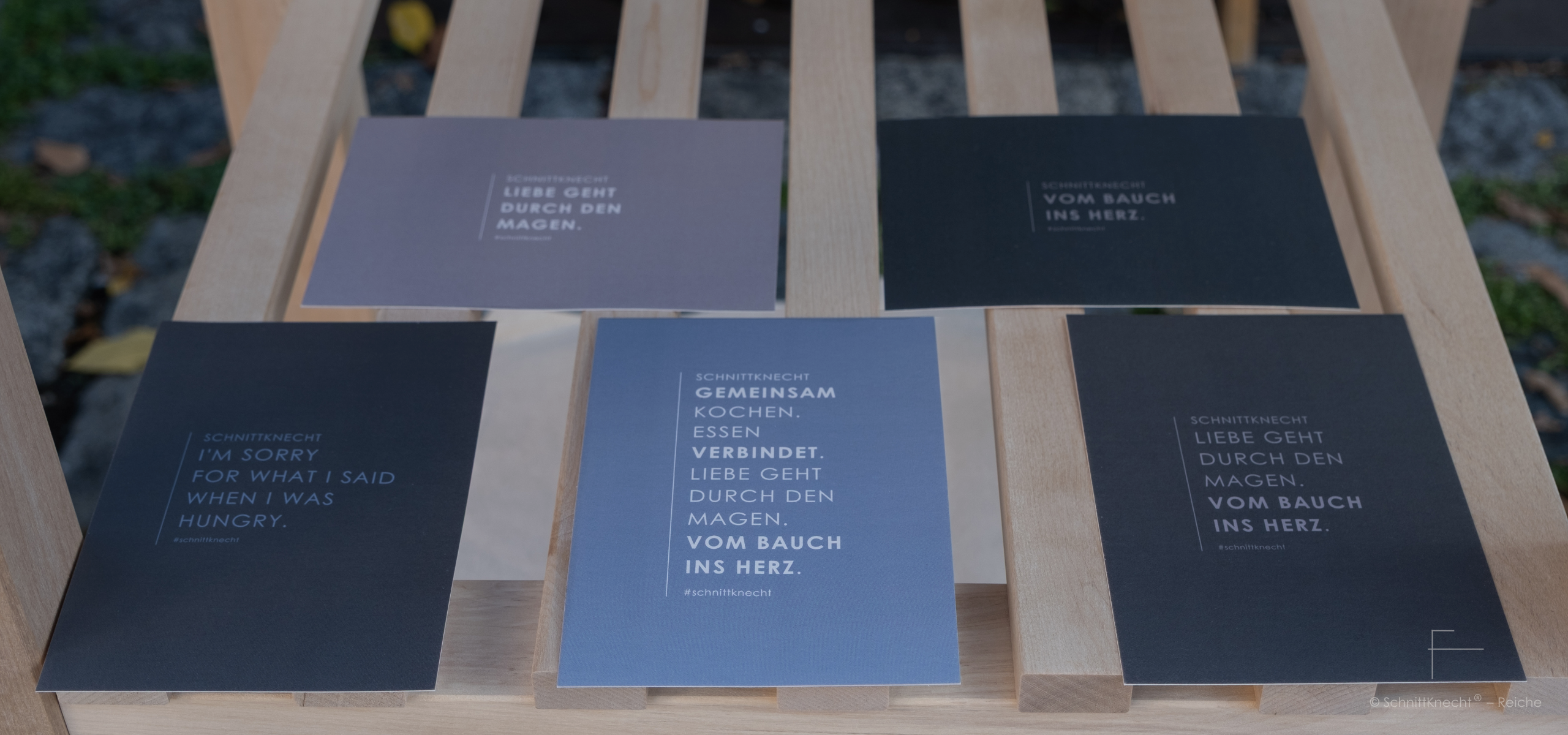 Schnittknecht® Postkarten auf Holztisch mit Sprüchen zu Kochen, Liebe und Essen wie Liebe geht durch den Magen