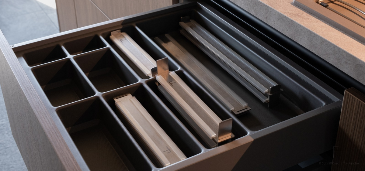 Kompakt zusammengebaute SchnittKnecht® Schneidebrett-Unterlage mit weiteren modularen Komponenten, platzsparend in einer Küchenschublade verstaut.