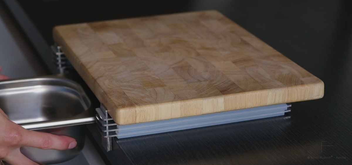 SchnittKnecht® Schneidebrett-Unterlage mit Holzschneidebrett, Ergonomie-Modulen und GN-Behälter auf dunkler Küchenarbeitsplatte.